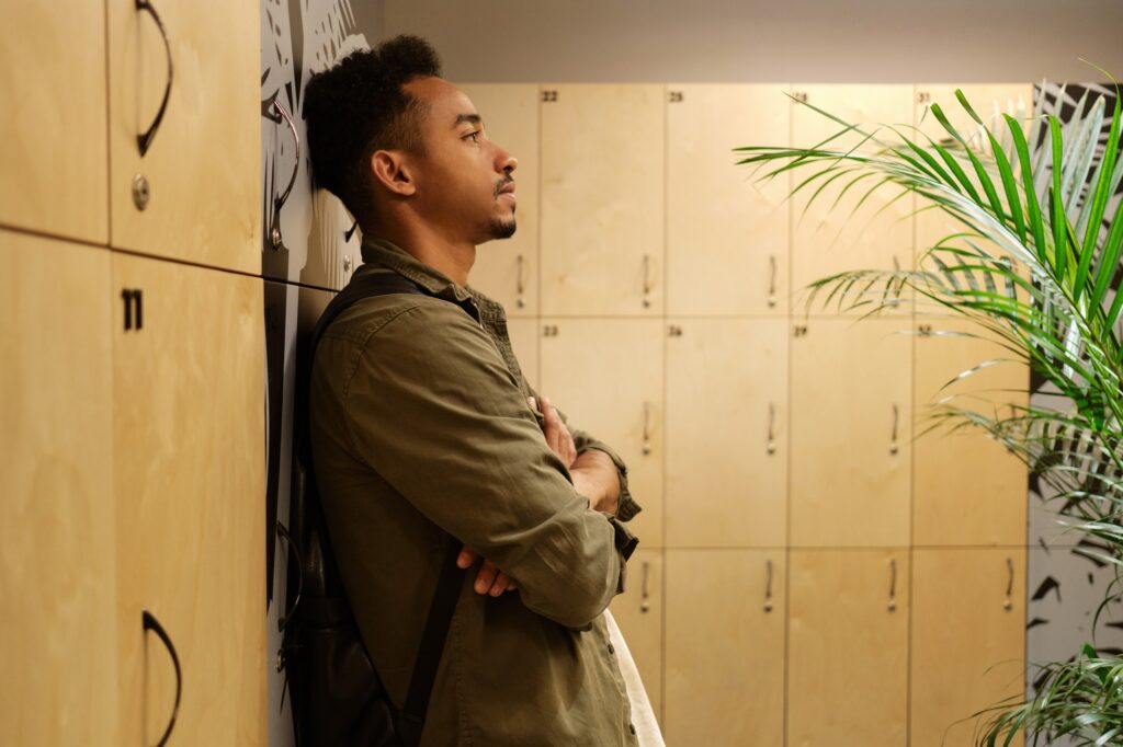 Young handsome casual African American man thoughtfully standing in locker room